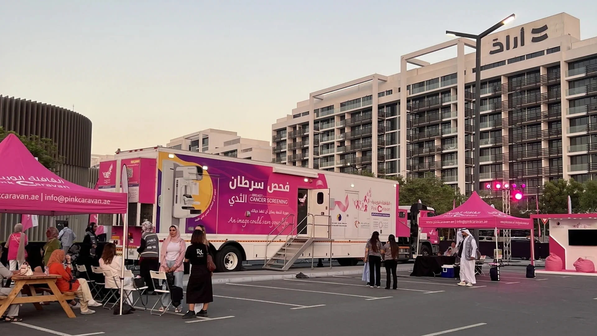 A mobile medical clinic and community event tents set up in a modern outdoor development during the evening.