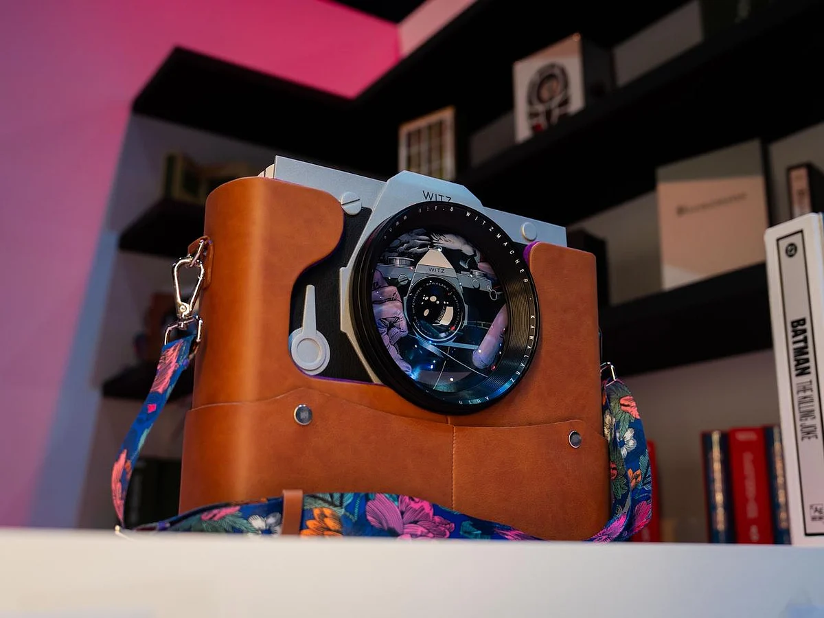 A heavy, camera-shaped comic book with aluminium covers and a detachable lens displayed on a stand.