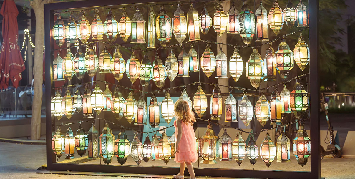 A festive outdoor market at Aljada with decorative lighting, kiosks, and families enjoying evening entertainment.