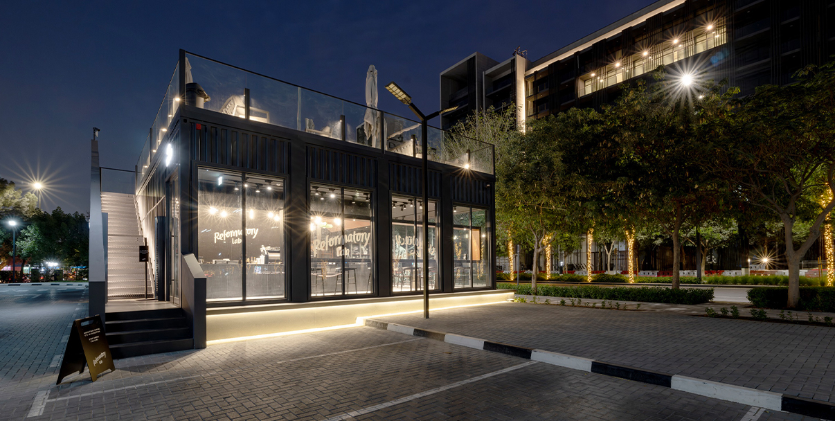 A modern coffee shop exterior with comic book style branding and an outdoor terrace in a contemporary urban development.